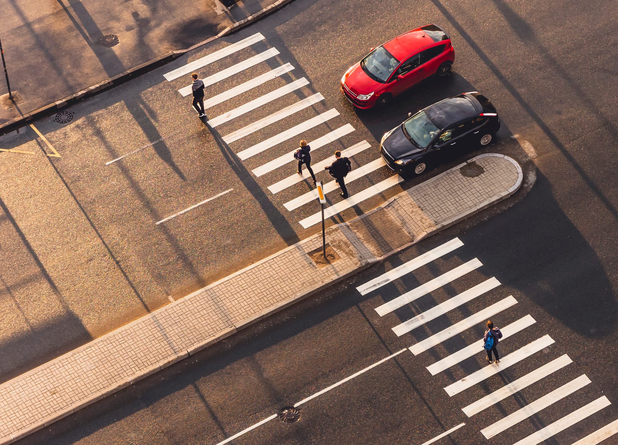 View from above of pedestrians crossing in a crosswalk with two cars stopped.