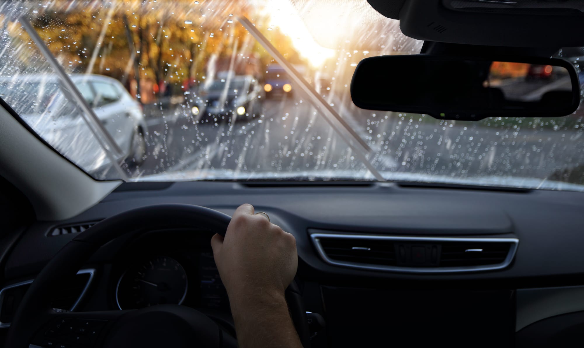 View of a driver's hand on the steering wheel of a vehicle driving in heavy rain.